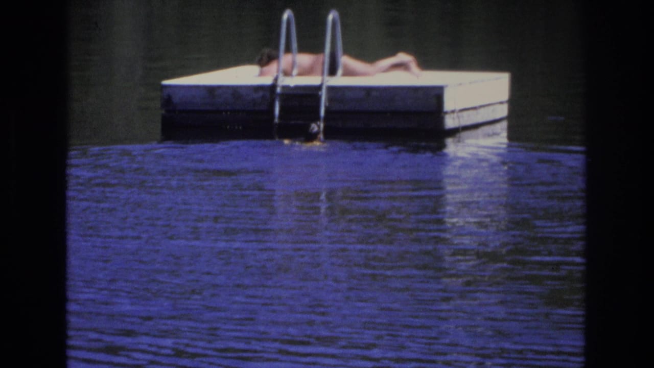 A person rests on a dock with a metal ladder rising from calm water.