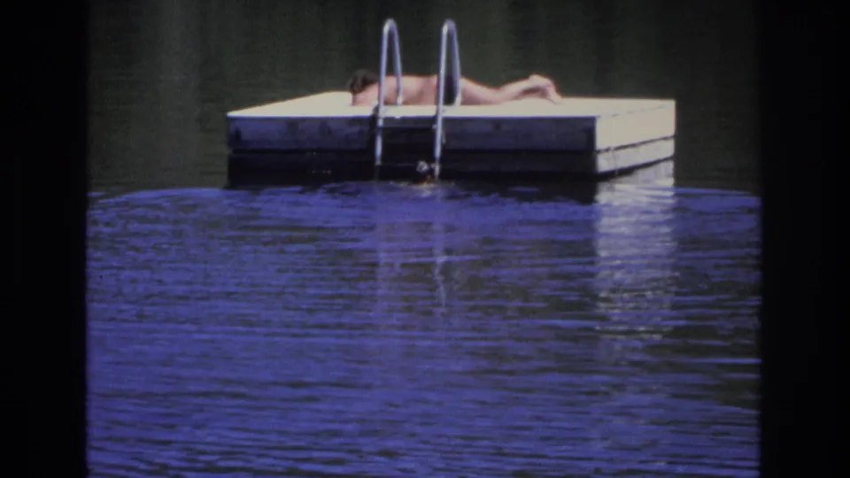 1968 Ocean City home-movie frame showing a dockside sunbather and ladder above dark blue rippling water.