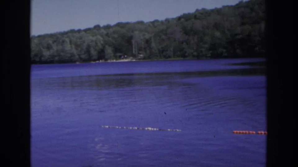 1968 8mm footage from Ocean City, New Jersey, showing purple-blue lake water, wooded hills, and a roped swimming line with buoys.