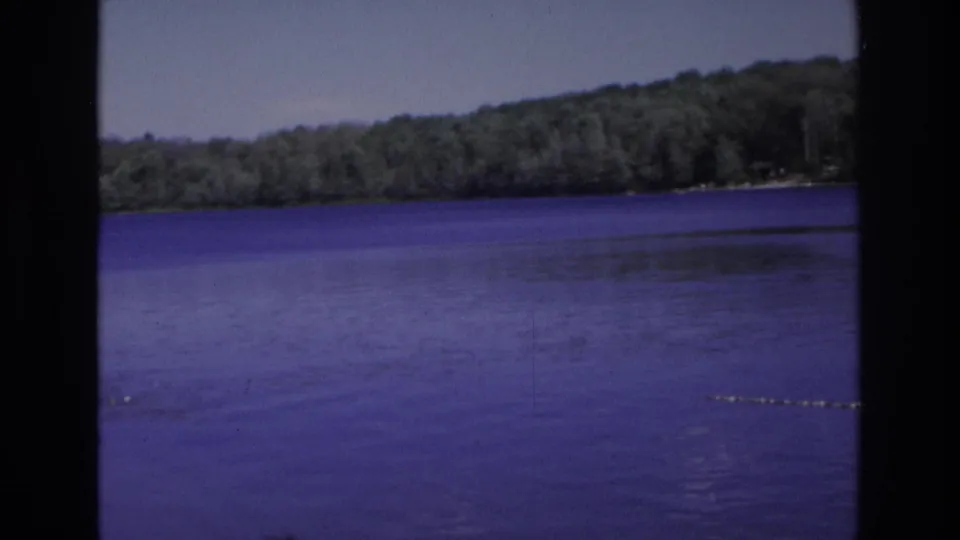 A wide 1968 lakeside view shows calm blue-purple water, distant wooded hills, and part of a roped swimming area.