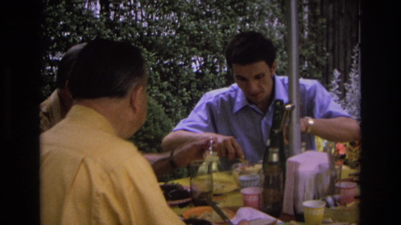 1968 Ocean City home-movie frame showing three adult men at an outdoor meal, with one man in a blue shirt eating across the table.