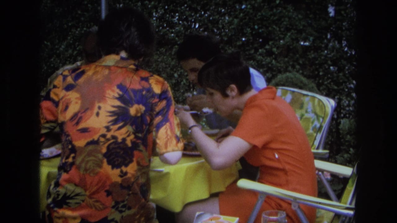 Three adults in 1968 Ocean City sit close together at an outdoor meal, with a yellow tablecloth and foliage in view.