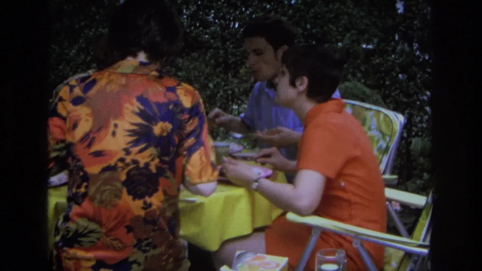 A candid 1968 home-movie frame shows adults eating at a yellow table in an outdoor Ocean City setting.