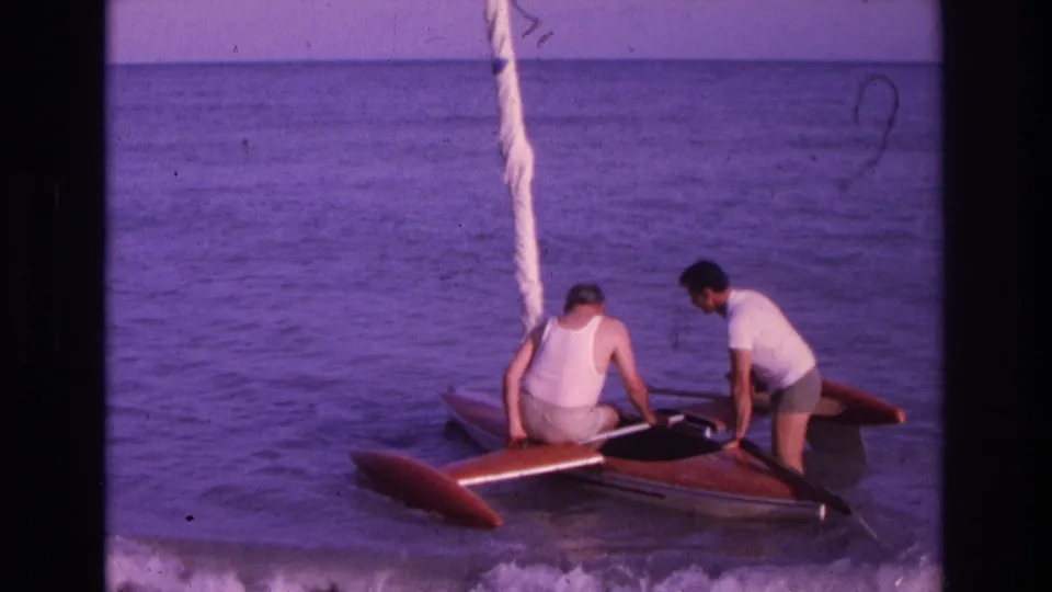 Two adult men work around a small sailboat or catamaran on the water, likely part of the same 1968 Ocean City reel.
