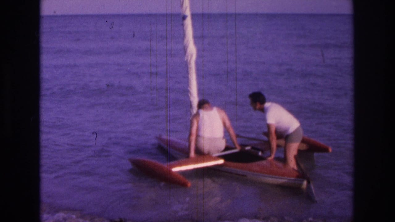 Two men steady a small red boat in shallow ocean water.