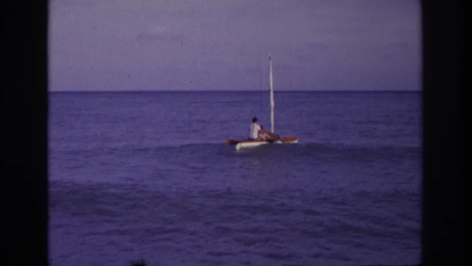 Distant 1968 Ocean City sailing view with two people seated on a small catamaran-style boat and a single white mast.