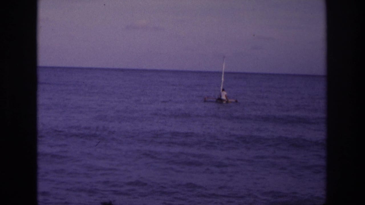 Distant person on a small sail raft on calm ocean water under an overcast sky.