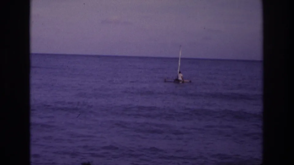 1968 Ocean City, New Jersey home-movie frame showing a distant person on a small sail raft beyond gentle ocean waves.