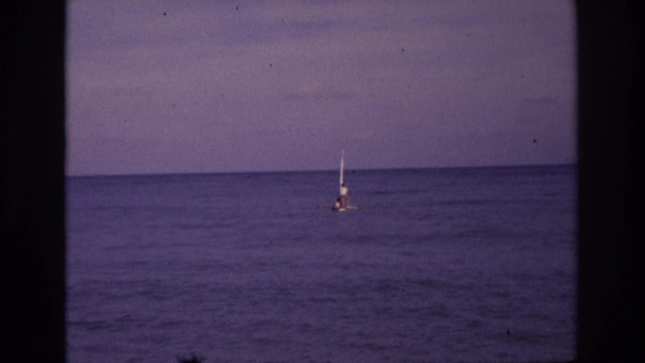 1968 Ocean City home-movie frame showing a distant small sailboat on calm ocean water under a muted dusk sky.