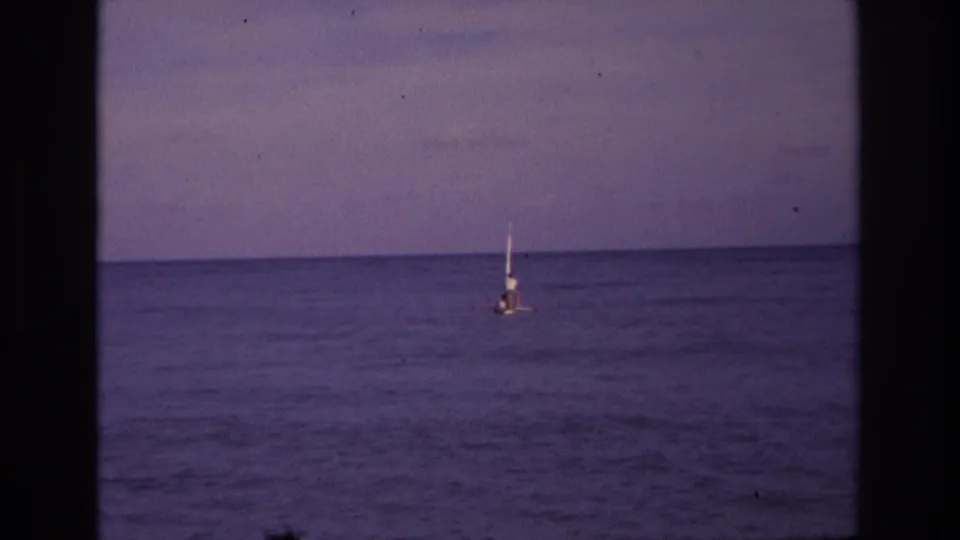 1968 Ocean City home-movie frame showing a distant small sailboat on calm ocean water under a muted dusk sky.