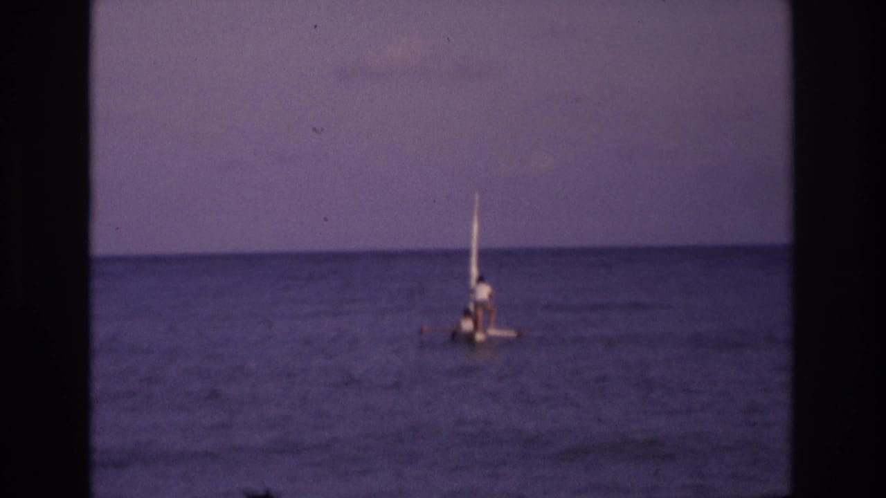 Small sailboat nearer the center of the frame on calm ocean water.
