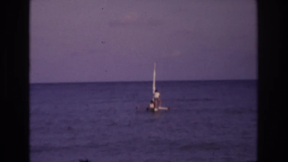 Ocean City, New Jersey 1968 footage frame with a small sailboat moving across calm blue water, filmed from shore or another distance.