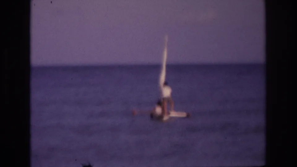 Ocean City 1968 frame of a seated man in a small sailboat, with a tall pale sail or mast and purple-blue home-movie color.
