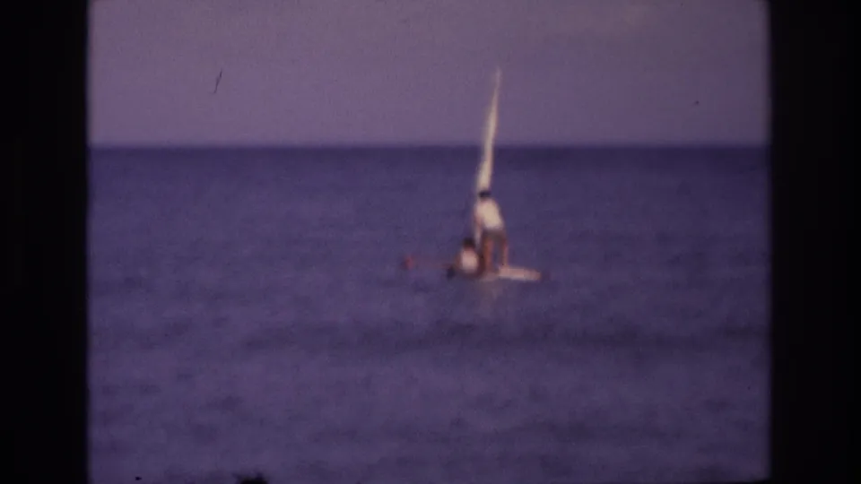 A distant 8mm view of a small sailboat offshore in Ocean City, New Jersey, with two people visible as the boat sits low in the water.