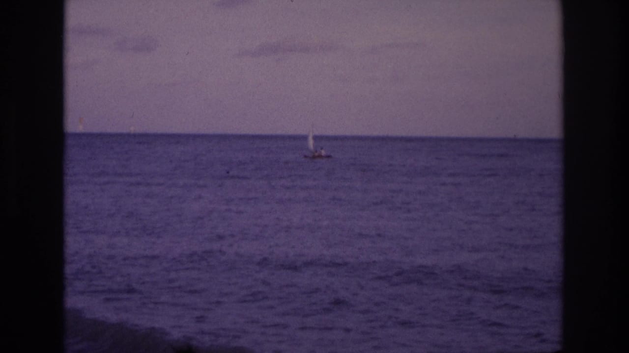 1968 Ocean City, New Jersey 8mm frame showing a small distant sailboat on calm purple-blue water under a muted sky.