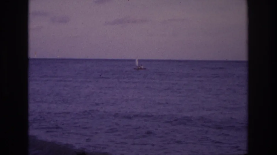 1968 Ocean City, New Jersey 8mm frame showing a small distant sailboat on calm purple-blue water under a muted sky.