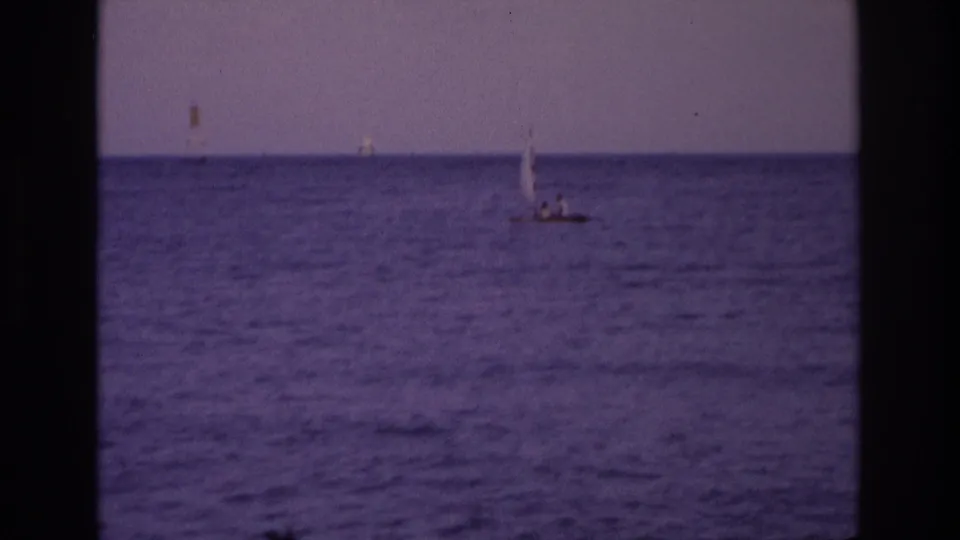 1968 Ocean City, New Jersey home-movie frame showing a small sailboat offshore beneath a hazy purple sky, with distant horizon markers.