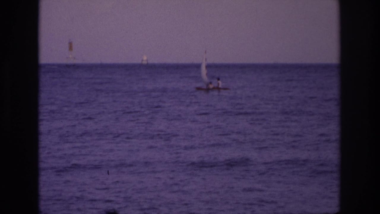 Small sailboat near the horizon on open water with dark vertical film border at left.