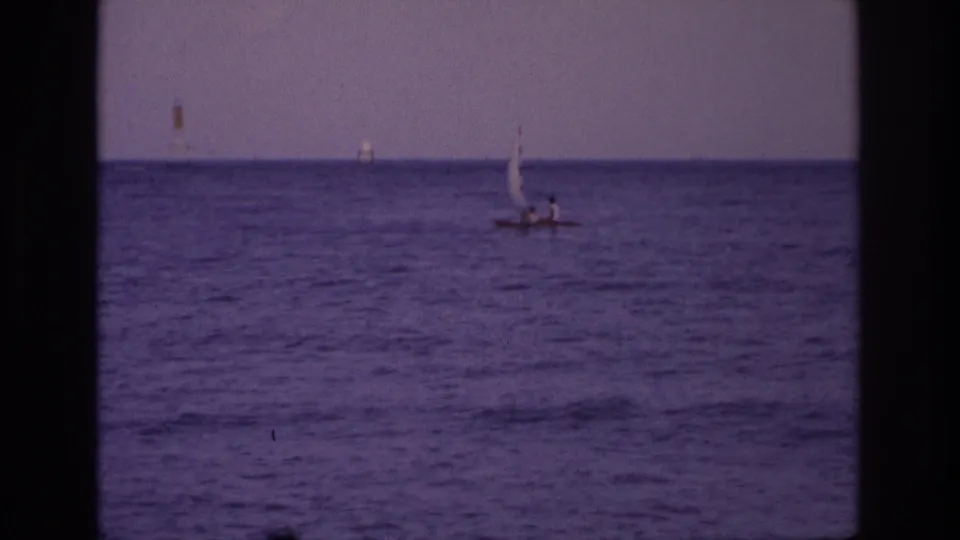 1968 Ocean City, New Jersey frame with a small sailboat gliding across open water, framed by dark 8mm gate edges and a hazy horizon.