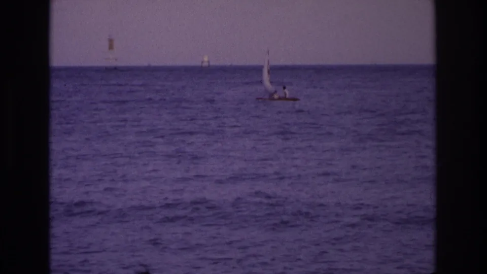 Ocean City, New Jersey 1968 home-movie still showing a small sailboat with two distant people against the ocean horizon.
