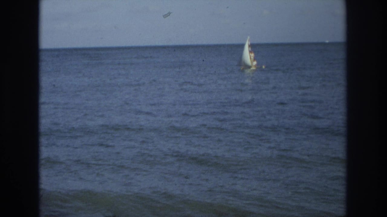 1968 8mm footage frame showing a small sailboat on calm ocean water near Ocean City, New Jersey, with pale sky above.