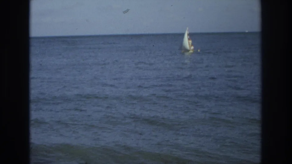 1968 8mm footage frame showing a small sailboat on calm ocean water near Ocean City, New Jersey, with pale sky above.