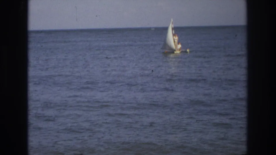 1968 8mm frame from Ocean City, New Jersey showing a small dinghy with a white sail moving across calm ocean water.