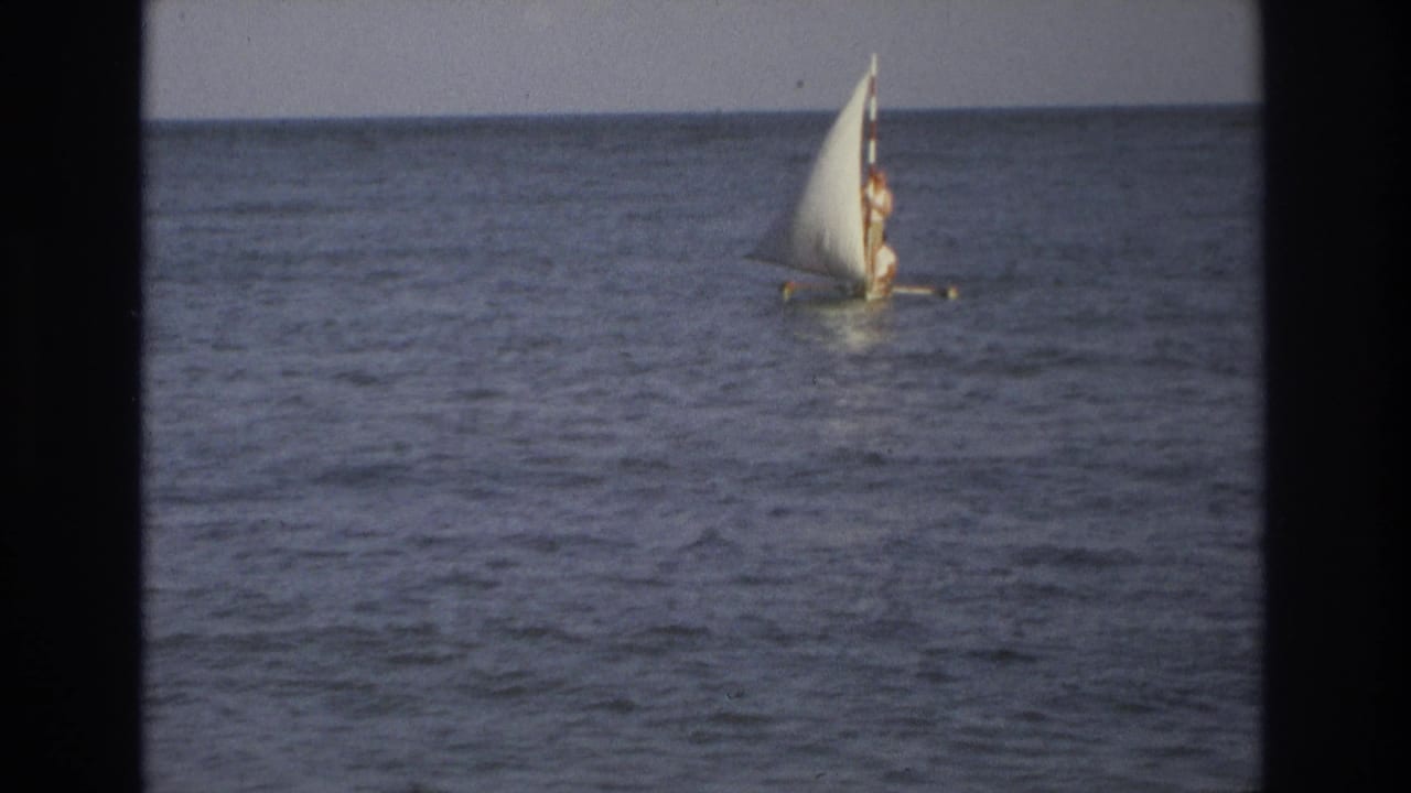 A distant sailor stands on a small sailboat off Ocean City, New Jersey, with the ocean horizon behind them.