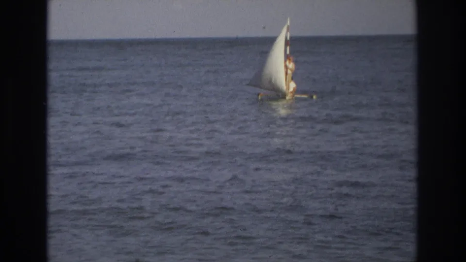 A distant sailor stands on a small sailboat off Ocean City, New Jersey, with the ocean horizon behind them.
