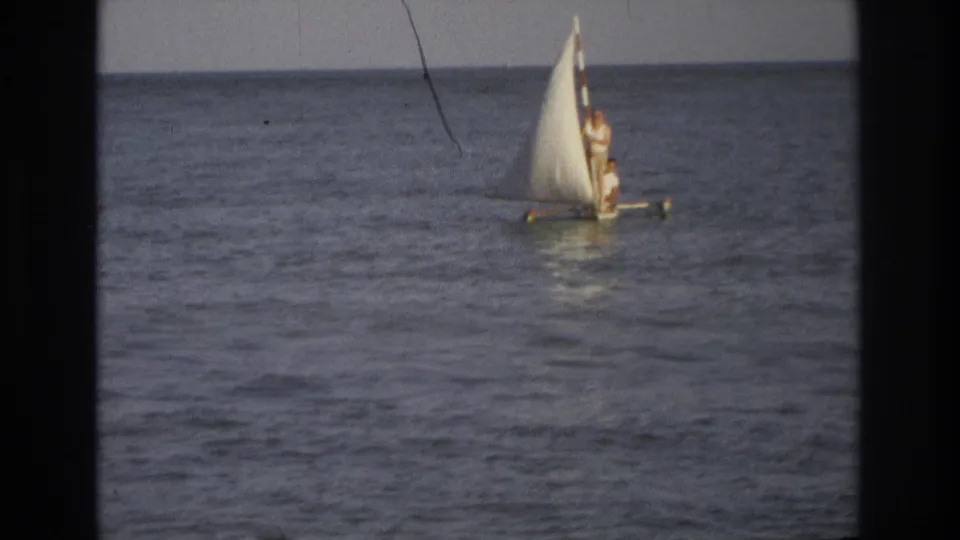 Ocean City 1968 8mm frame showing a small sailboat on open water, with a standing person and visible film wear.