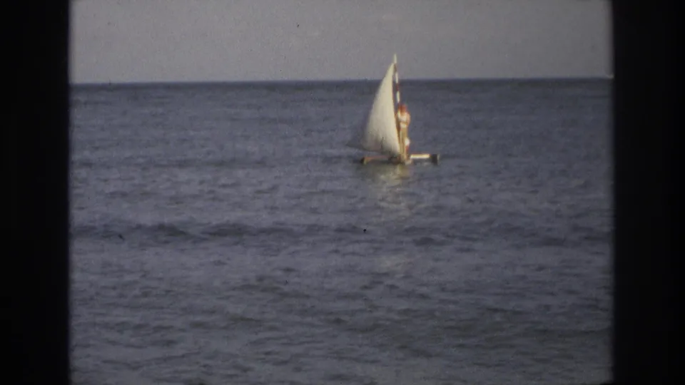 1968 Ocean City, New Jersey 8mm frame showing a small white sailboat with a distant rider bobbing on open water.