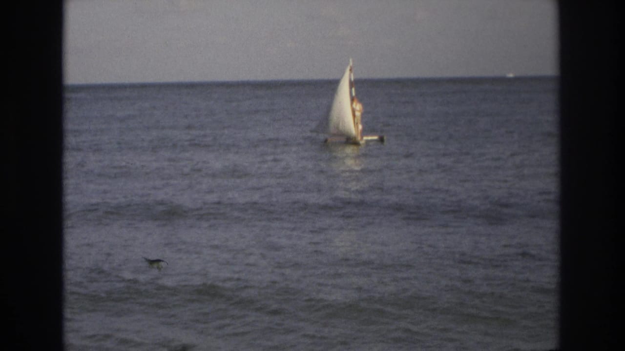 Small sailboat farther out on the ocean with waves in the foreground.