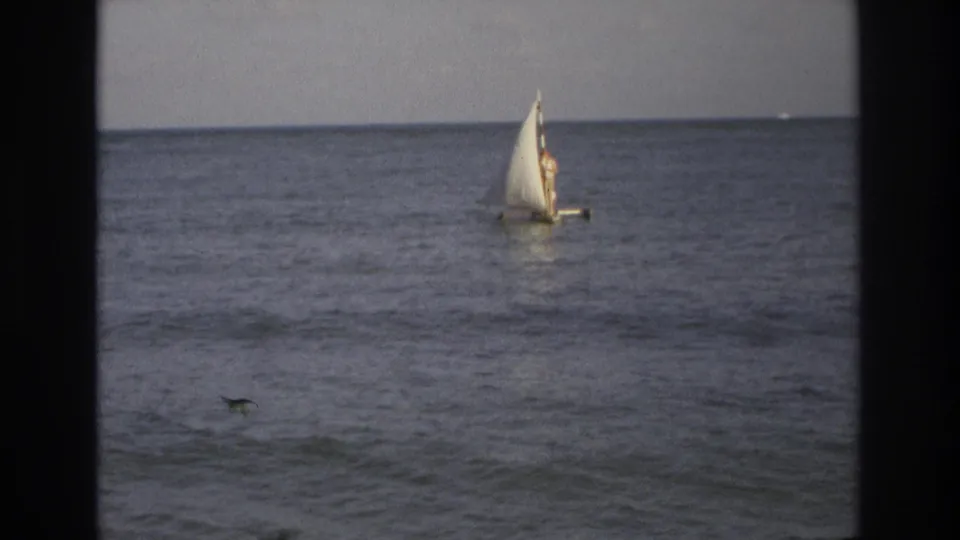 1968 Ocean City, New Jersey home-movie frame of a distant small sailboat moving across calm ocean water.