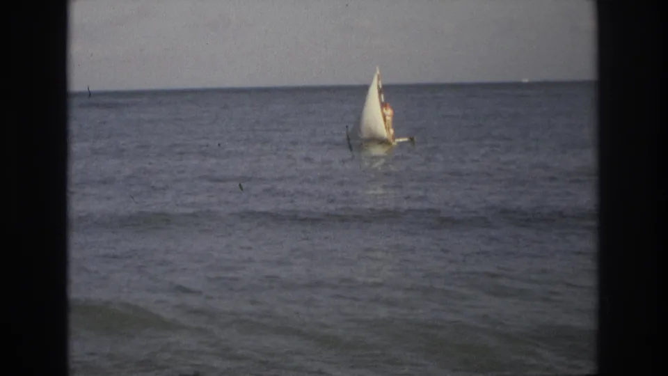 1968 Ocean City, New Jersey 8mm still showing a small sailboat and distant rider amid low coastal waves.