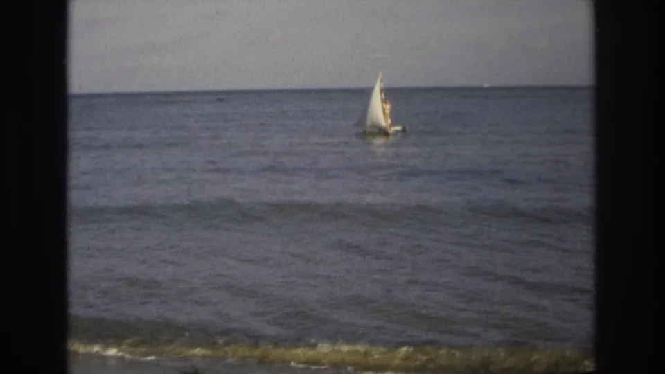 1968 Ocean City, New Jersey 8mm frame showing a small white sailboat offshore on calm water under a muted sky.