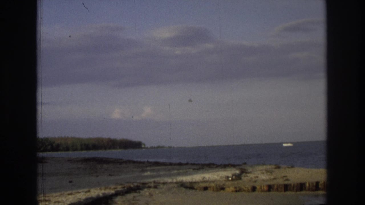 1968 Ocean City, New Jersey frame with the ocean, low tree-lined shore, cloudy sky, dark scan borders, and a small pale object appearing near the distant horizon.