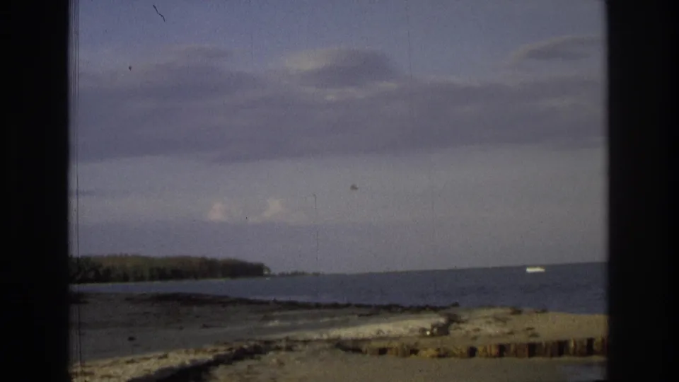 1968 Ocean City, New Jersey frame with the ocean, low tree-lined shore, cloudy sky, dark scan borders, and a small pale object appearing near the distant horizon.