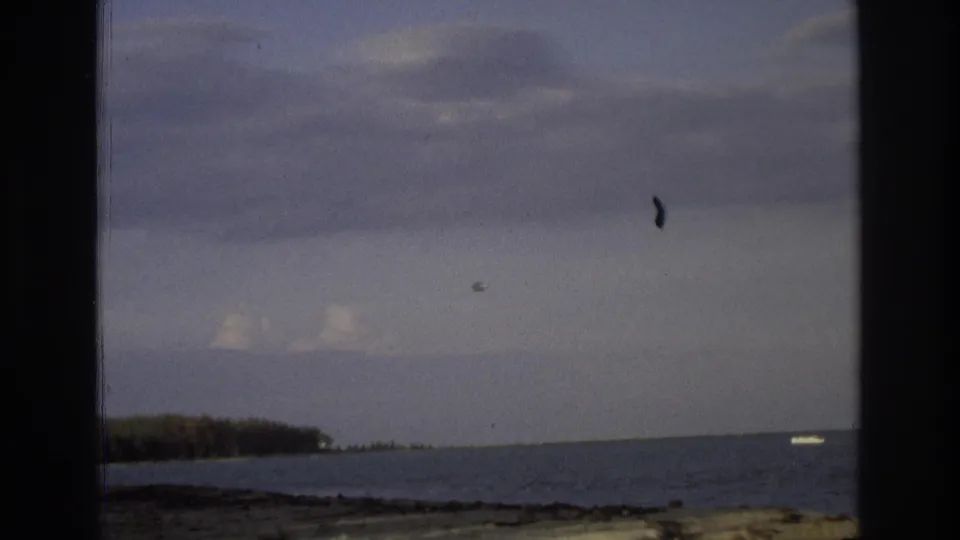 1968 Ocean City, New Jersey 8mm frame showing a cropped coastal horizon with cloudy sky, dark shoreline, water, and a small pale object near the right side of the frame.