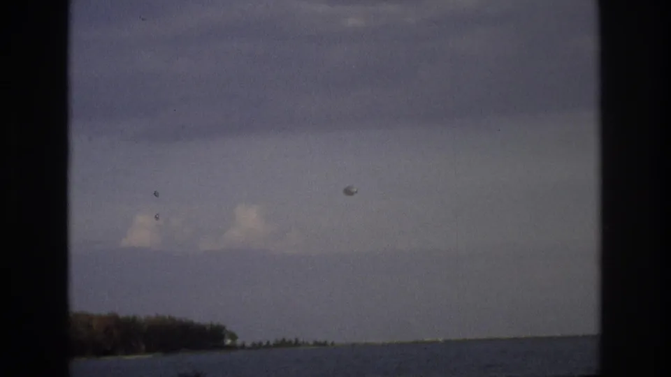 Muted 8mm frame from Ocean City in 1968 showing ocean horizon, shoreline trees, aircraft, and a round sky object.