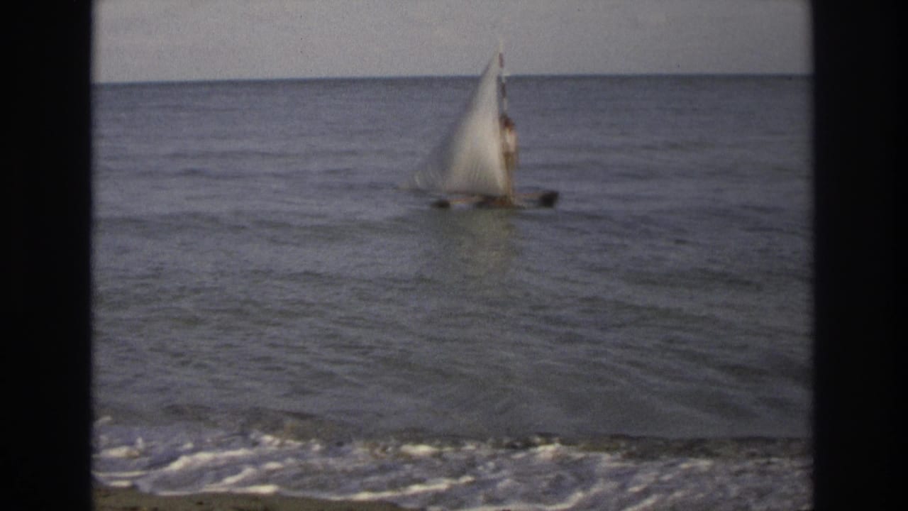 White-sailed boat farther offshore on calm water with low waves at the beach.