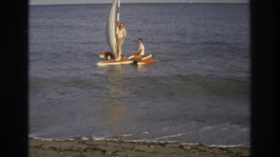Two men appear aboard a small recreational sailboat off Ocean City, New Jersey, with the white sail raised over calm water.