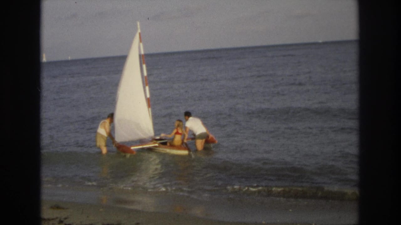 A group steadies a mini sailboat as a wave reaches the shore.