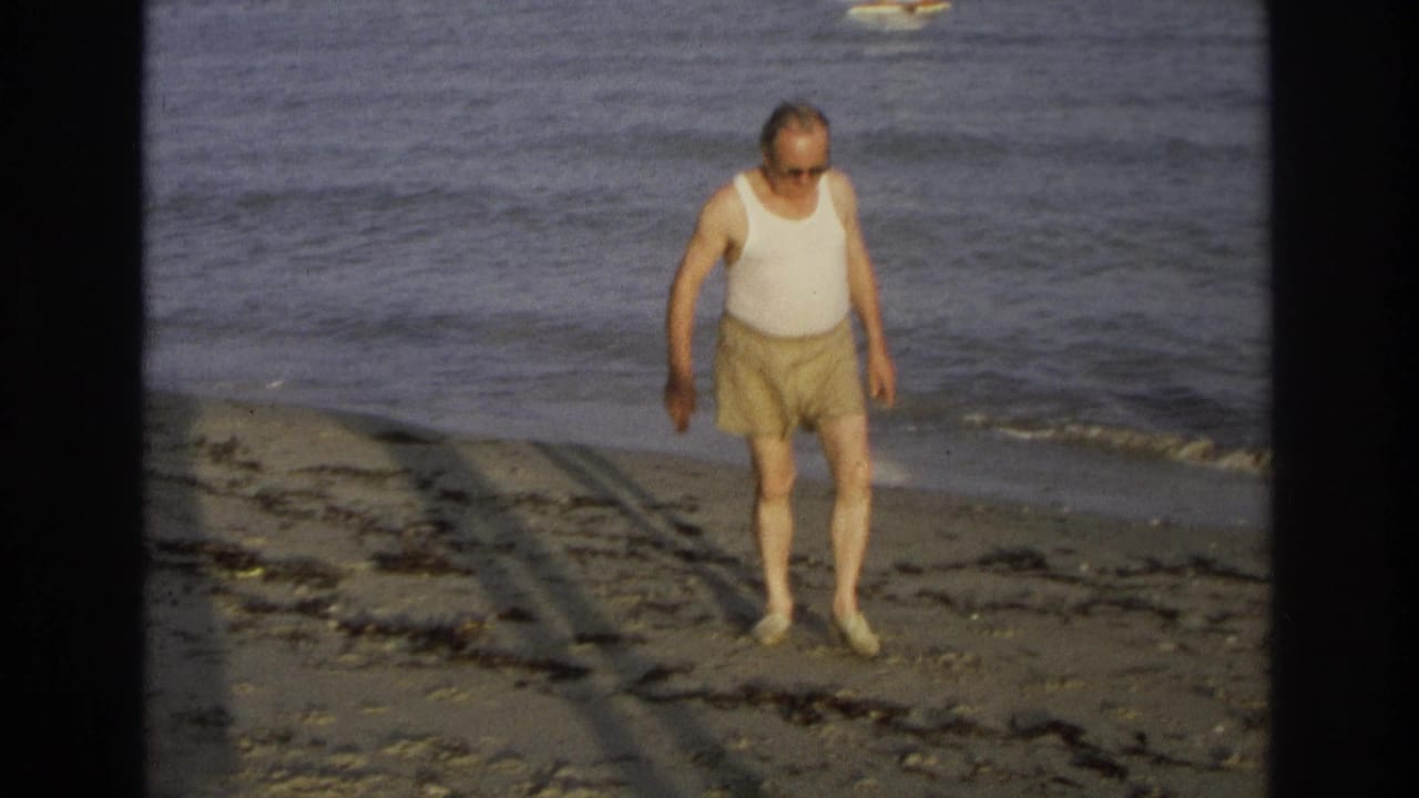 Older man in sunglasses walks on a sandy beach near the ocean.