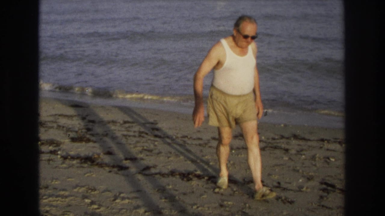 Older man in sunglasses and beach clothes moves along the Ocean City shoreline in 1968 home-movie footage.
