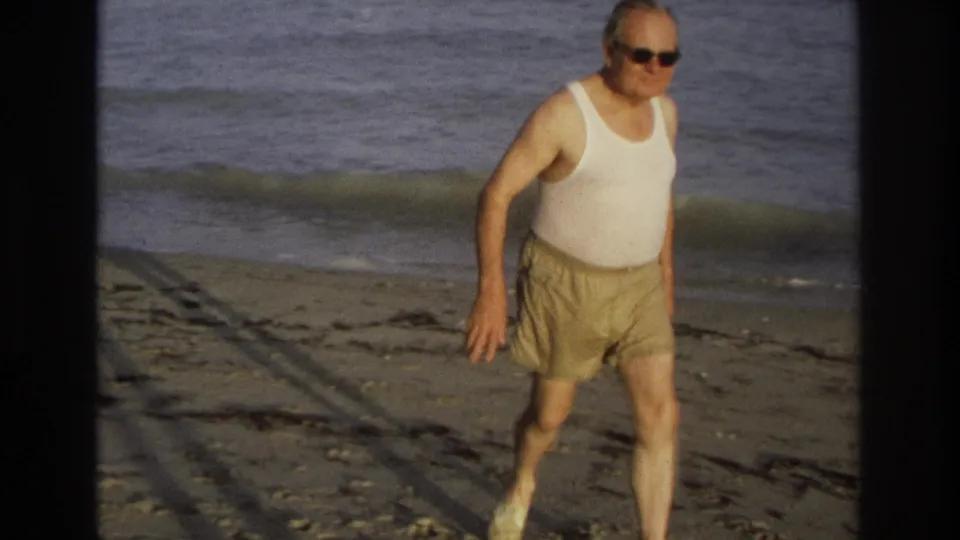 Closer 8mm frame of the older beachgoer walking on Ocean City sand, with waves rolling in behind him.