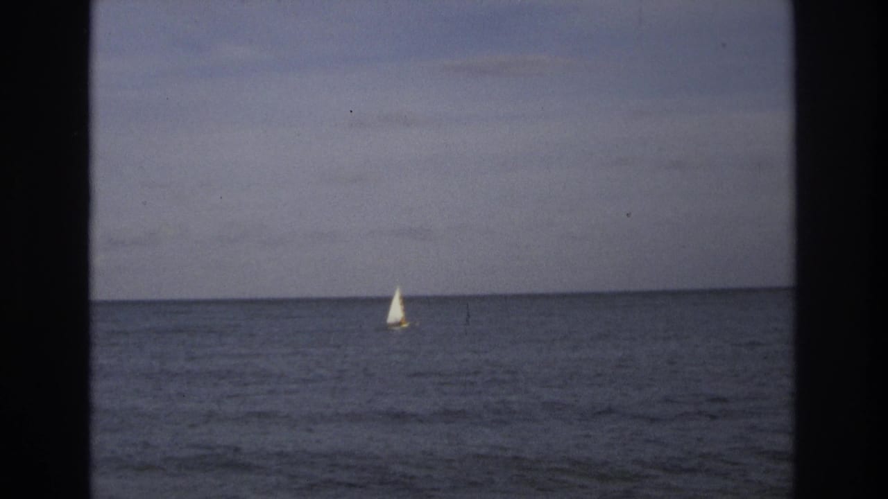 Distant sailboat on calm ocean near Ocean City, New Jersey in 1968 home-movie footage, with muted sky and visible film-gate edges.