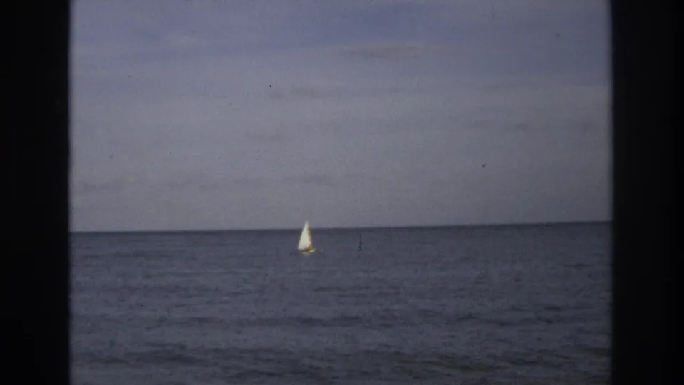 Distant sailboat on calm ocean near Ocean City, New Jersey in 1968 home-movie footage, with muted sky and visible film-gate edges.