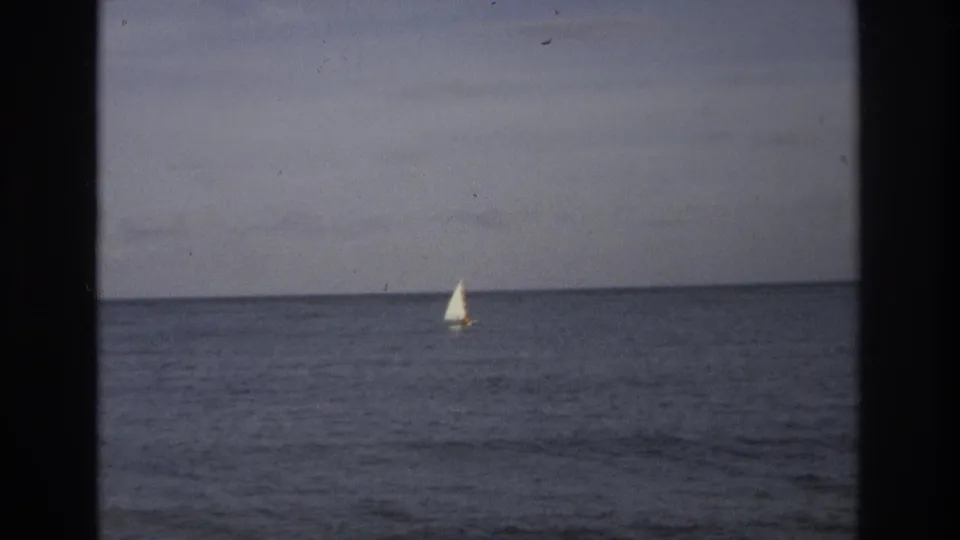 A small sailboat appears far out on the Ocean City waterline in 1968 8mm footage, bordered by the dark contact-sheet frame.