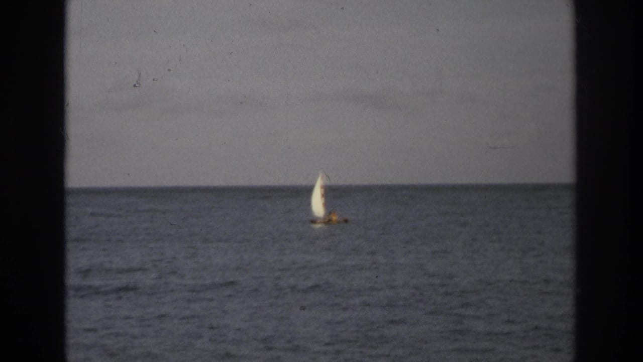 1968 Ocean City, New Jersey 8mm frame showing a distant small sailboat crossing calm ocean water under a gray sky.