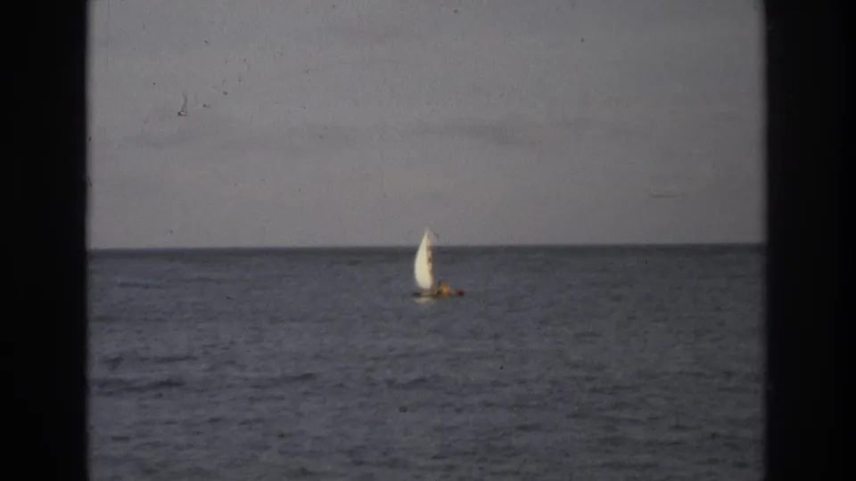 1968 Ocean City, New Jersey 8mm frame showing a distant small sailboat crossing calm ocean water under a gray sky.
